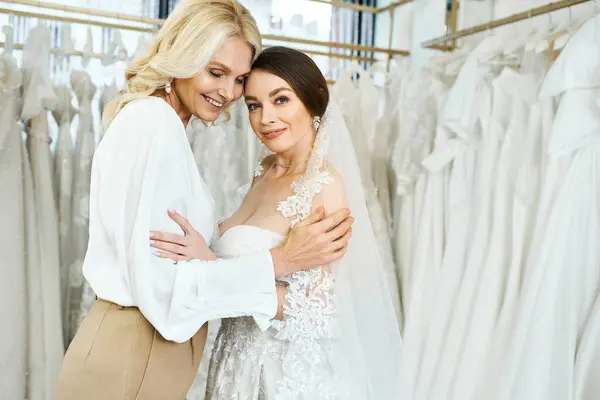 Молодая брюнетка невеста и ее мать среднего возраста стоят в свадебном салоне, осматривая стойку красивых платьев. — стоковое фото