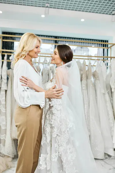 Eine junge brünette Braut im Brautkleid und ihre Mutter mittleren Alters stehen nebeneinander in einem Brautsalon. — Stockfoto