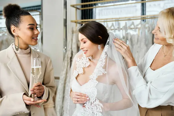 Dos mujeres, una una joven novia con un vestido blanco, y la otra su madre, de pie cerca de un estante de vestidos en un salón de novias. - foto de stock