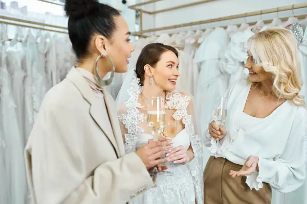 Дві жінки, молода наречена у весільній сукні та її мати середнього віку у сукні для наречених, стоять разом, тримаючи шампанські окуляри. — стокове фото