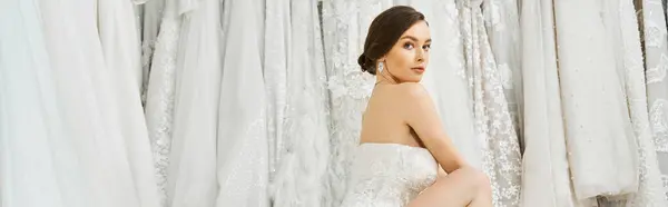 Молодая брюнетка невеста элегантно позирует в белом платье в свадебном салоне, источая очарование и изящество. — стоковое фото