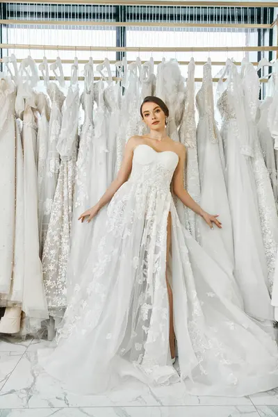Uma jovem morena cercada por um rack de vestidos elegantes em um salão de casamento, contemplando suas opções para o grande dia. — Fotografia de Stock