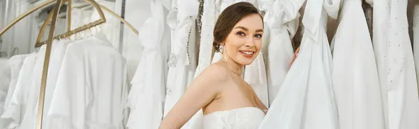 Молода, красива наречена стоїть перед стійкою суконь у весільному салоні, вибираючи її ідеальну сукню. — стокове фото