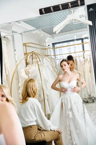 A young, beautiful bride in a white dress standing in front of a mirror, admiring her reflection in a wedding salon. — Stock Photo