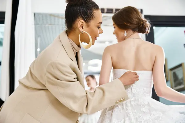 Молода брюнетка наречена в білій сукні і подружка нареченої в бежевому костюмі стоять разом у весільному салоні, виключаючи елегантність. — стокове фото