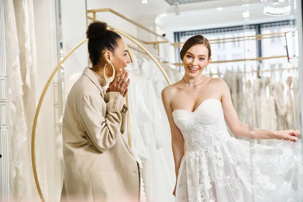 A young brunette woman stands beside a beautiful bride in a white dress in a wedding salon. — Stock Photo
