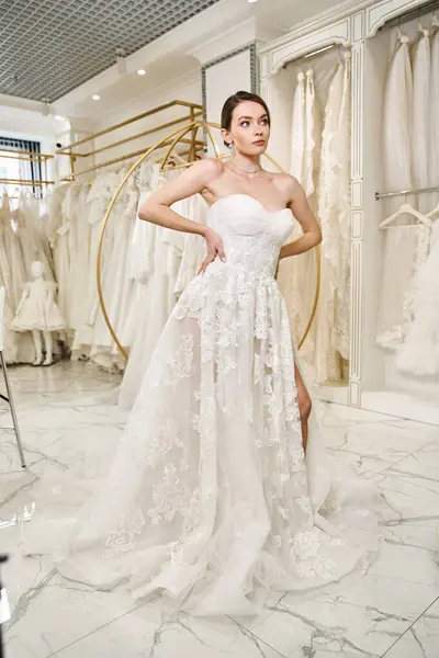 Eine junge, schöne Braut steht in einem Hochzeitssalon, umgeben von einer Reihe weißer Kleider, und betrachtet ihre Wahl. — Stockfoto