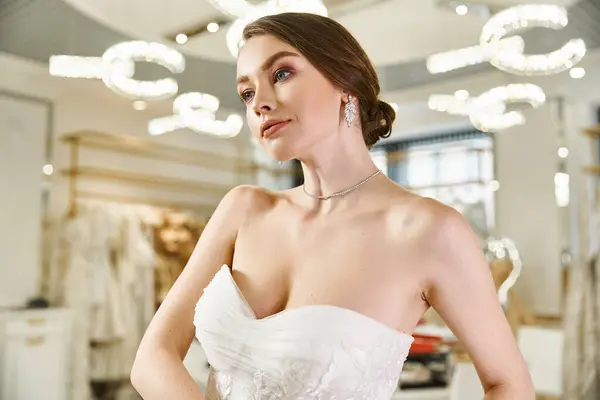 Uma noiva jovem e bonita em um vestido branco olha para seu reflexo em um espelho em um salão de casamento. — Fotografia de Stock