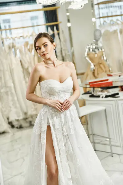 Молодая брюнетка невеста в белом платье смотрит на свое отражение в зеркале в свадебном салоне, воплощая элегантность и изящество. — стоковое фото
