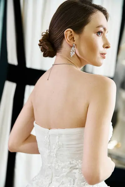 Una giovane sposa bruna in un abito da sposa bianco ammirando il suo riflesso in uno specchio in un salone di nozze. — Stock Photo
