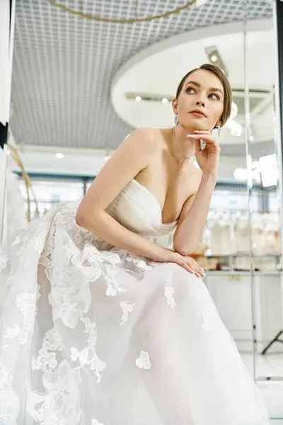 Una giovane sposa bruna in un abito bianco fluente siede elegantemente su una sedia in un salone di nozze. — Foto stock