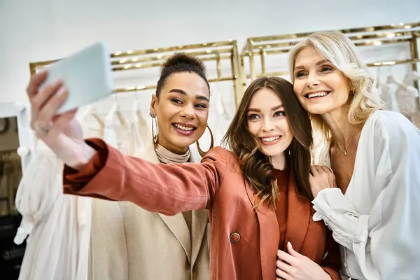 Dos mujeres jóvenes, una futura novia y su mejor amiga, posan mientras toman una selfie en una tienda de ropa de moda. - foto de stock