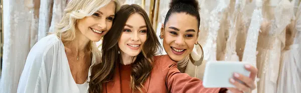 Tres mujeres, una joven novia hermosa, su madre y su mejor amiga, tomando una selfie con un teléfono celular. - foto de stock