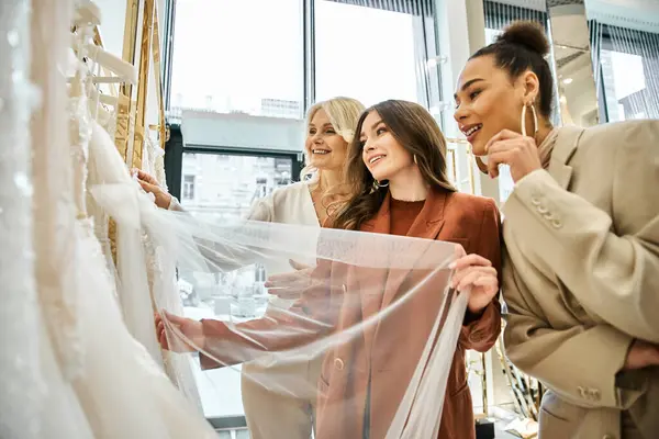 Uma jovem noiva, sua mãe e melhor amiga estão unidos na frente de uma seleção de vestidos. — Fotografia de Stock