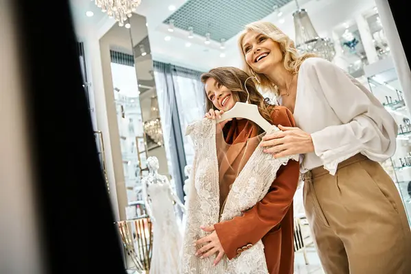 Una sposa e sua madre stanno elegantemente fianco a fianco durante lo shopping per il perfetto abito da sposa. — Foto stock