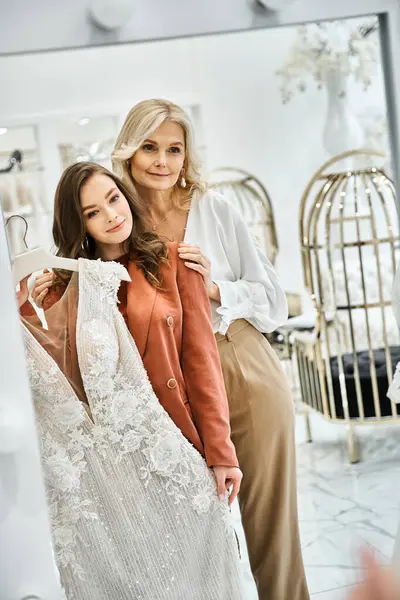 Two women, a young bride and her mother, stand next to each other in front of a mirror, browsing wedding attire. — Stock Photo
