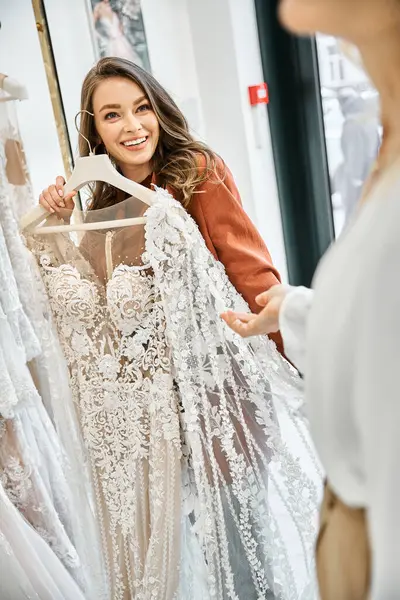 Uma noiva jovem e bonita fica com sua mãe na frente de um rack de vestidos, selecionando cuidadosamente o vestido de casamento perfeito.. — Fotografia de Stock