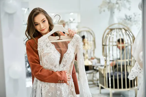 Una hermosa joven está sosteniendo un vestido de novia en una tienda - foto de stock