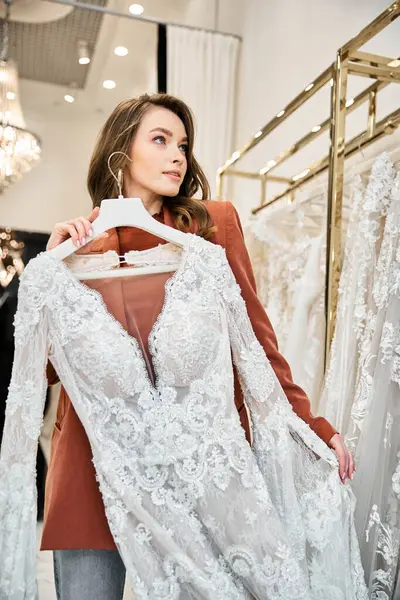 A young bride contemplates a stunning dress in a store filled with wedding attire. — Stock Photo