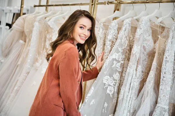 Eine junge schöne Braut steht vor einem Regal mit eleganten Brautkleidern und wählt sorgfältig das perfekte aus. — Stockfoto