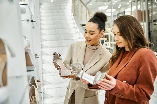 Two women, a young beautiful bride and her best friend, evaluate footwear in a store filled with a variety of shoes. — Stock Photo