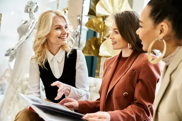 Trois femmes, dont une jeune belle mariée, conversent devant des mannequins tout en faisant du shopping pour son ensemble de mariage. — Photo de stock