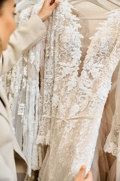 Uma noiva jovem, examina cuidadosamente um vestido em um rack em uma boutique nupcial. — Fotografia de Stock