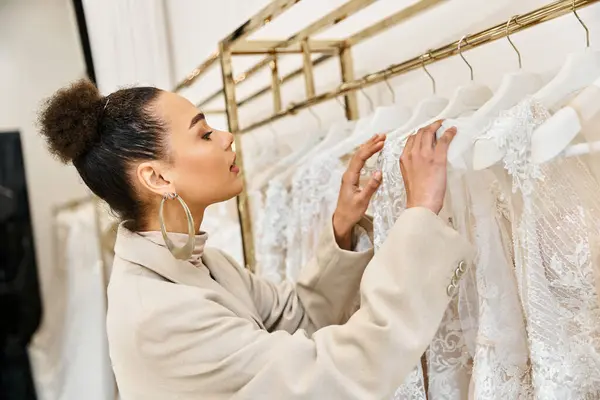 A young beautiful bride browses wedding dresses on a rack in a bridal store. — Stock Photo