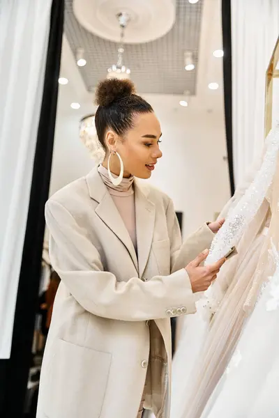 Une jeune belle mariée debout à côté d'une robe de mariée blanche, dans une boutique de mariée. — Photo de stock