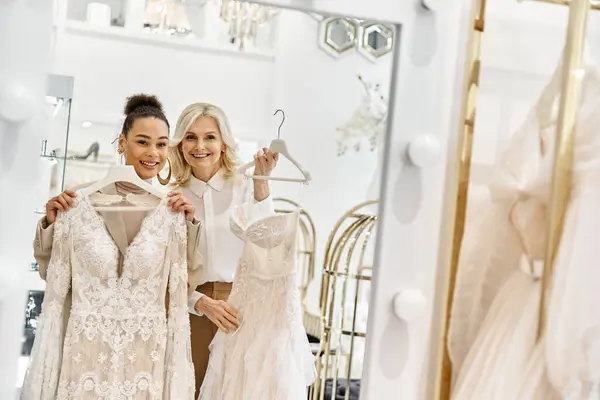 Dos mujeres, una novia joven y un asistente de tienda, se paran frente a un espejo evaluando el atuendo de la boda.. - foto de stock
