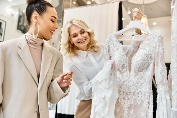Due giovani donne valutano attentamente un abito da sposa, discutendo dettagli di design e vestibilità perfetta per il giorno speciale.. — Foto stock