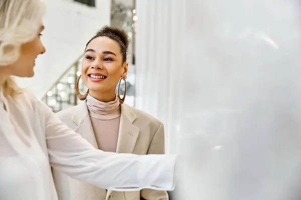 Two women dressed elegantly stand together looking at each other, possibly shopping for a wedding attire. — Stock Photo