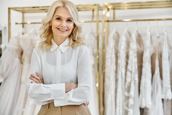 A middle-aged, beautiful shopping assistant stands in front of a rack of wedding dresses in a luxurious bridal salon. — Stock Photo