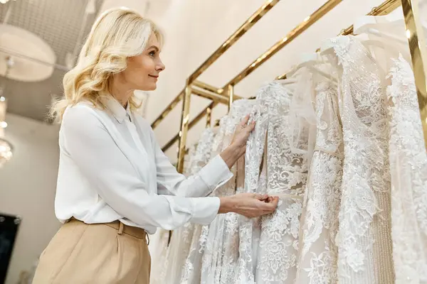 Um belo assistente de compras de meia-idade ajuda uma mulher a navegar através de vestidos de noiva em um rack em um salão de noivas. — Fotografia de Stock