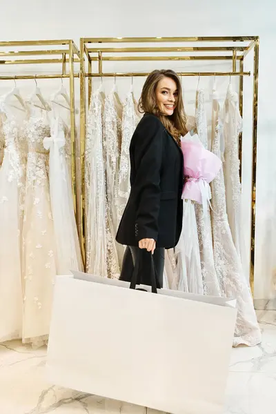 Una joven novia morena se para frente a un estante de vestidos en un salón de bodas, tratando de decidir sobre su vestido perfecto. - foto de stock