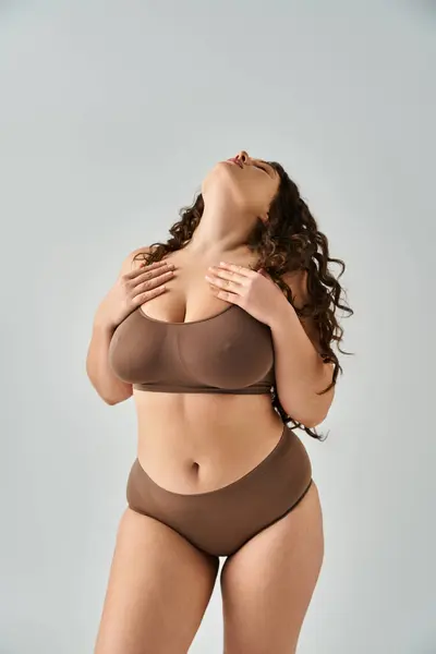 Attractive plus size girl in underwear putting head to behind and touching to neckline with hands — Stock Photo