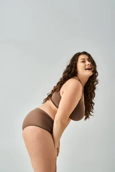 Cheerful plus size woman in underwear with curly brown hair laughing and leaning forward sideways — Stock Photo