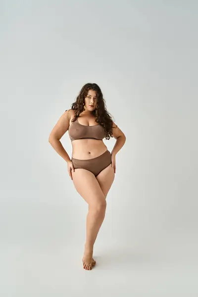 Attrayant curvy jeune femme en sous-vêtements posant avec les mains sur les hanches en arrière-plan gris — Photo de stock