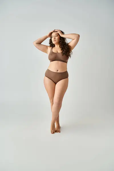 Beautiful curvy woman in underwear putting hands on head and looking to side in grey background — Stock Photo