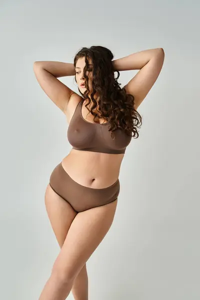 Alluring curvy girl in underwear putting hands on head and looking to down in grey background — Stock Photo