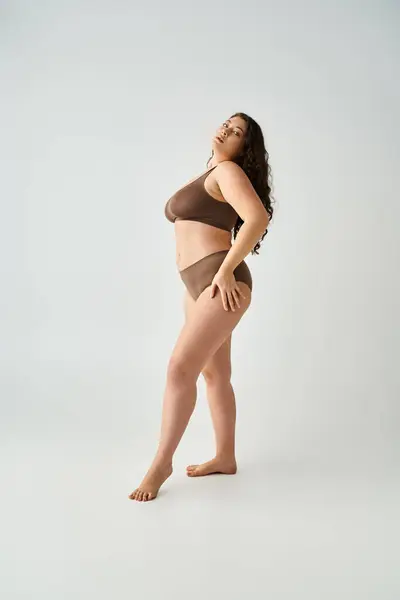Pretty plus size woman in underwear with hands on hips putting foot forward on grey background — Stock Photo