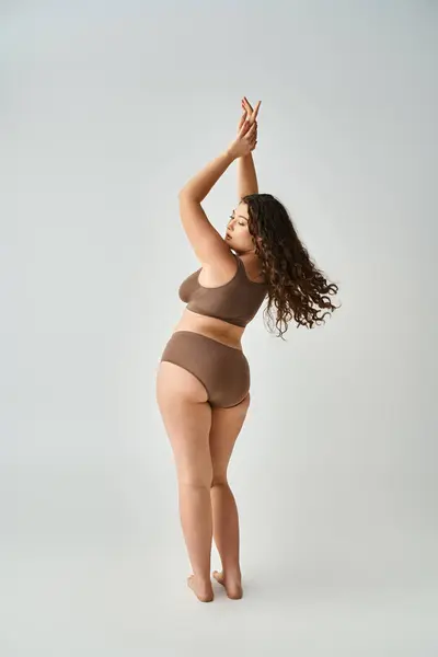 Séduisante femme courbée en sous-vêtements avec les cheveux bruns bouclés posant du dos et mettant les mains vers le haut — Photo de stock