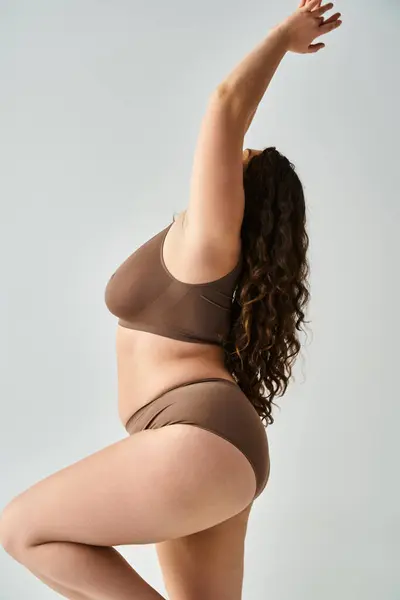 From sideways plus size young woman in underwear with curly brown hair putting hands to up — Stock Photo