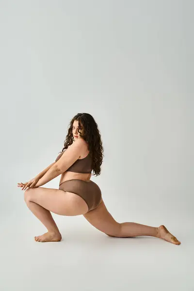 Beautiful plus size woman in underwear with curly brown hair posing from sideways with legs — Stock Photo
