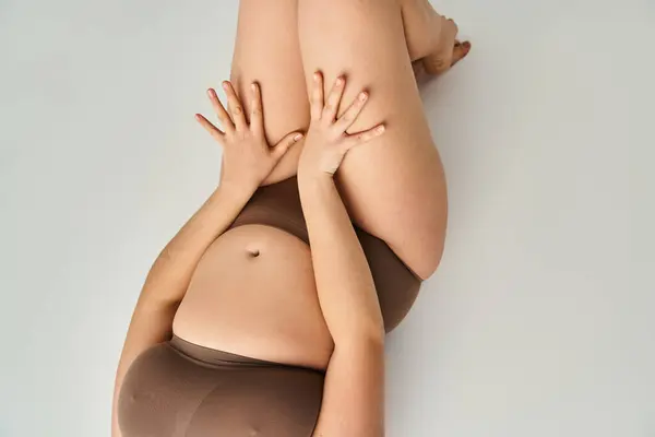 Cropped shot of body plus size young girl in brown underwear with hands on thighs on grey background — Stock Photo