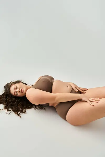 Séduisante plus la taille jeune femme en sous-vêtements marron avec les mains sur les hanches et les yeux fermés — Photo de stock