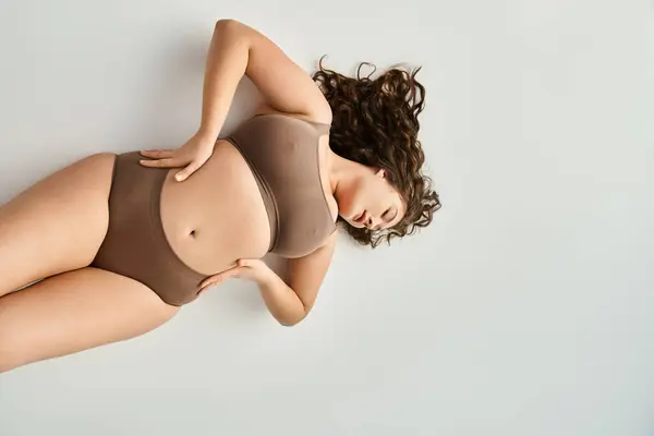 Plus size young girl in brown underwear with hands on waist and closed eyes leaning head — Stock Photo
