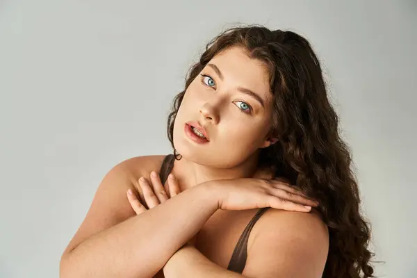 Retrato de mujer con curvas de unos 20 años con cabello castaño rizado y ojos azules cubriendo las manos hasta el escote - foto de stock