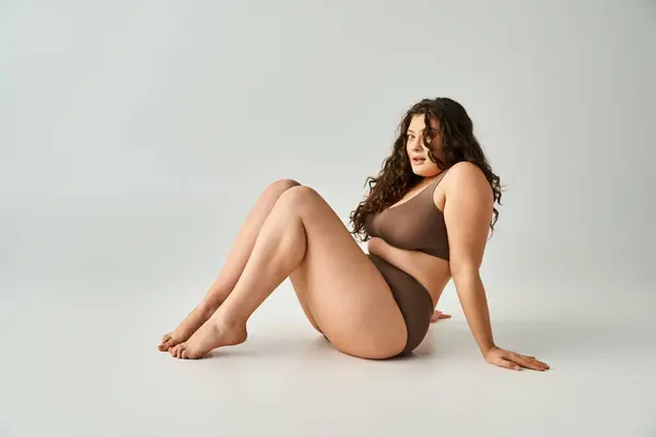 Attraktive Plus-Size-Frau in brauner Unterwäsche sitzend, an Arme gelehnt und Beine zu sich hochziehend — Stockfoto