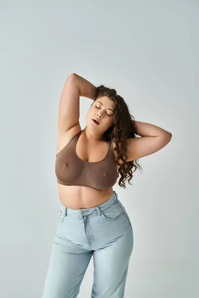 Attractive plus size woman in brown bra and blue jeans with closed eyes putting hands behind head — Stock Photo